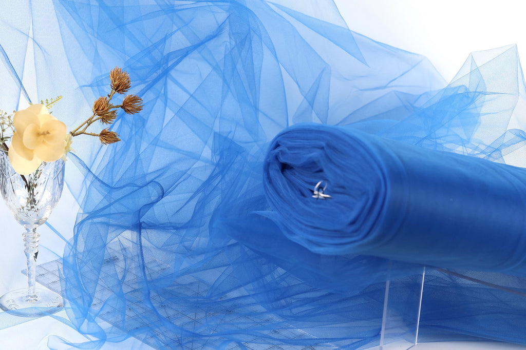 a blue tulle fabric, a glass vase with a single yellow flower, and a clear plastic stand with a rolled-up blue fabric on it.