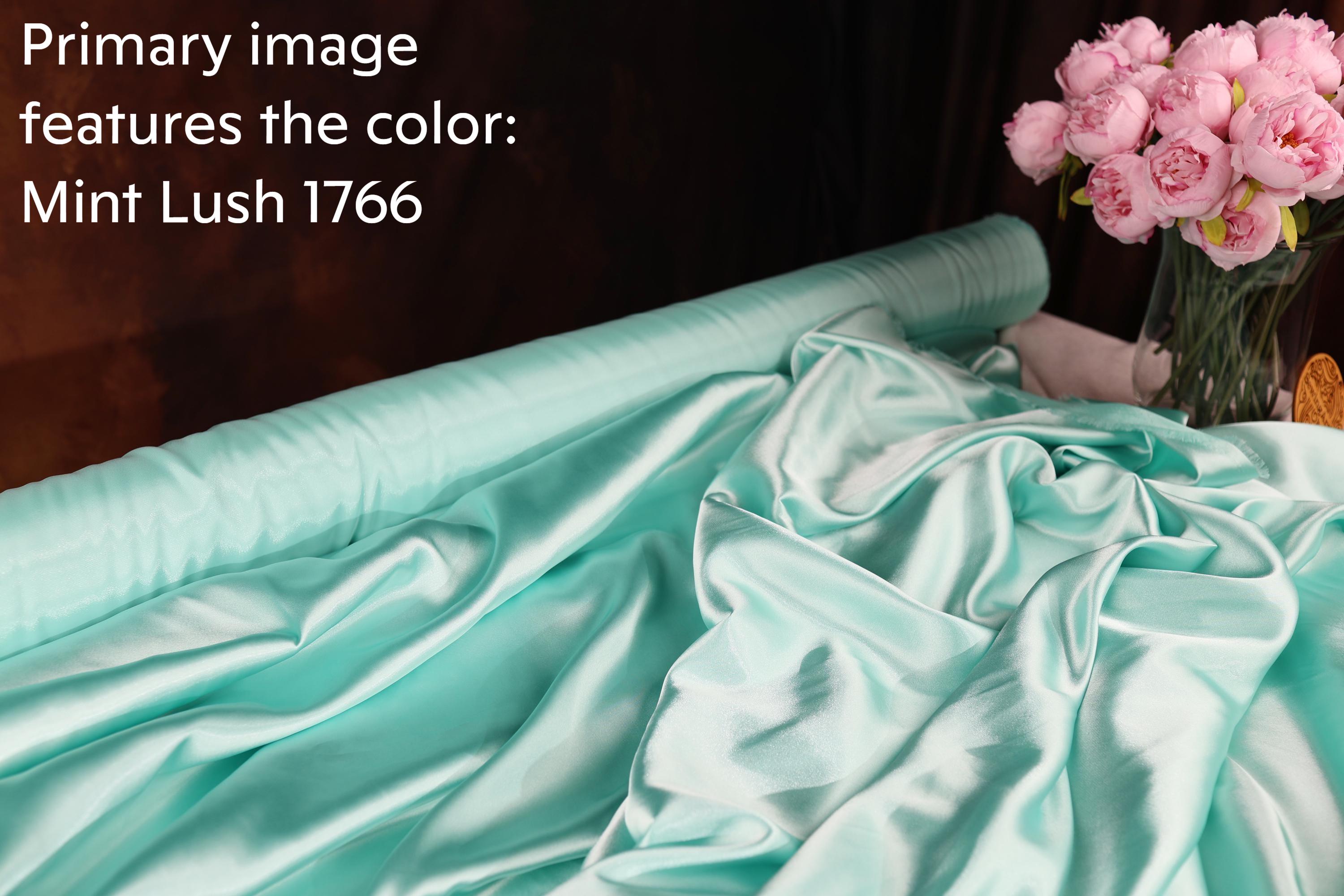 a roll of mint-colored satin fabric, with a vase of pink roses placed next to it.