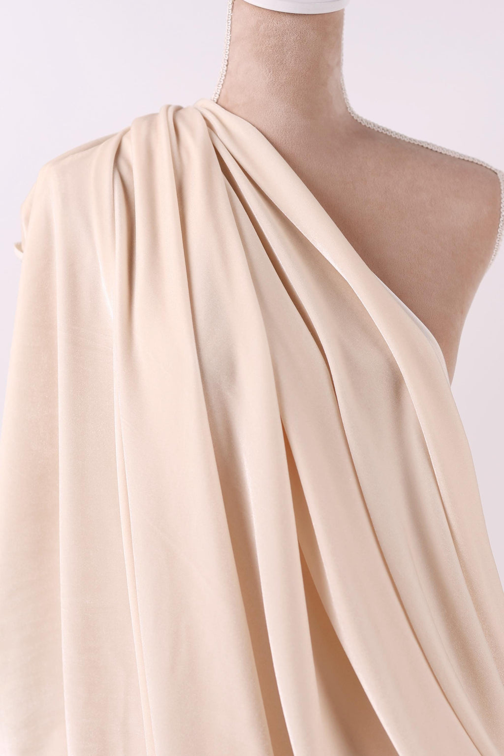 A mannequin wearing a beige, draped fabric draped over its shoulder.