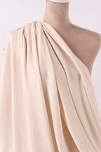 A mannequin wearing a beige, draped fabric draped over its shoulder.