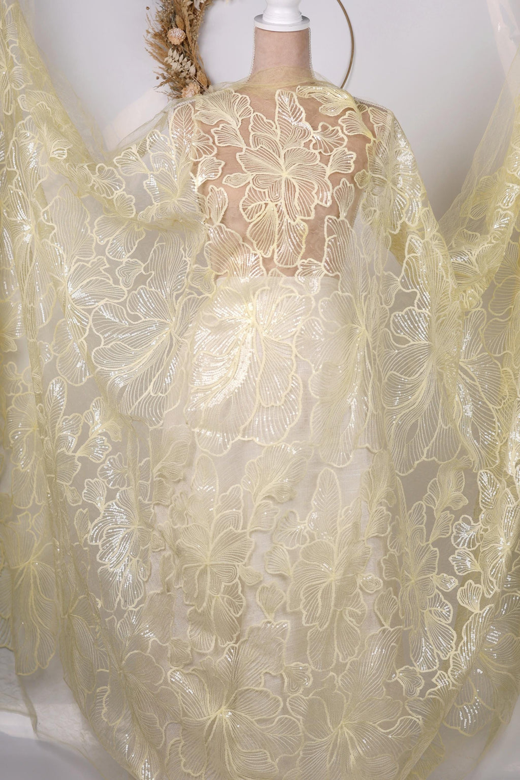A white mannequin wearing a yellow dress with a sheer, lace-like fabric draped over it.