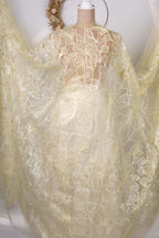 A white mannequin wearing a yellow dress with a sheer, lace-like fabric draped over it.