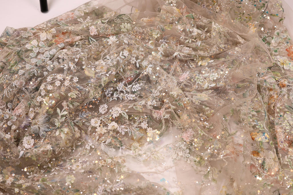 a close-up view of a delicate, intricately embroidered fabric with a floral pattern. The fabric appears to be made of sheer material, giving it a delicate and ethereal appearance. The embroidery features a variety of flowers and leaves, creating a visually appealing and detailed design. The fabric is spread out, allowing for a comprehensive view of its intricate details and patterns.