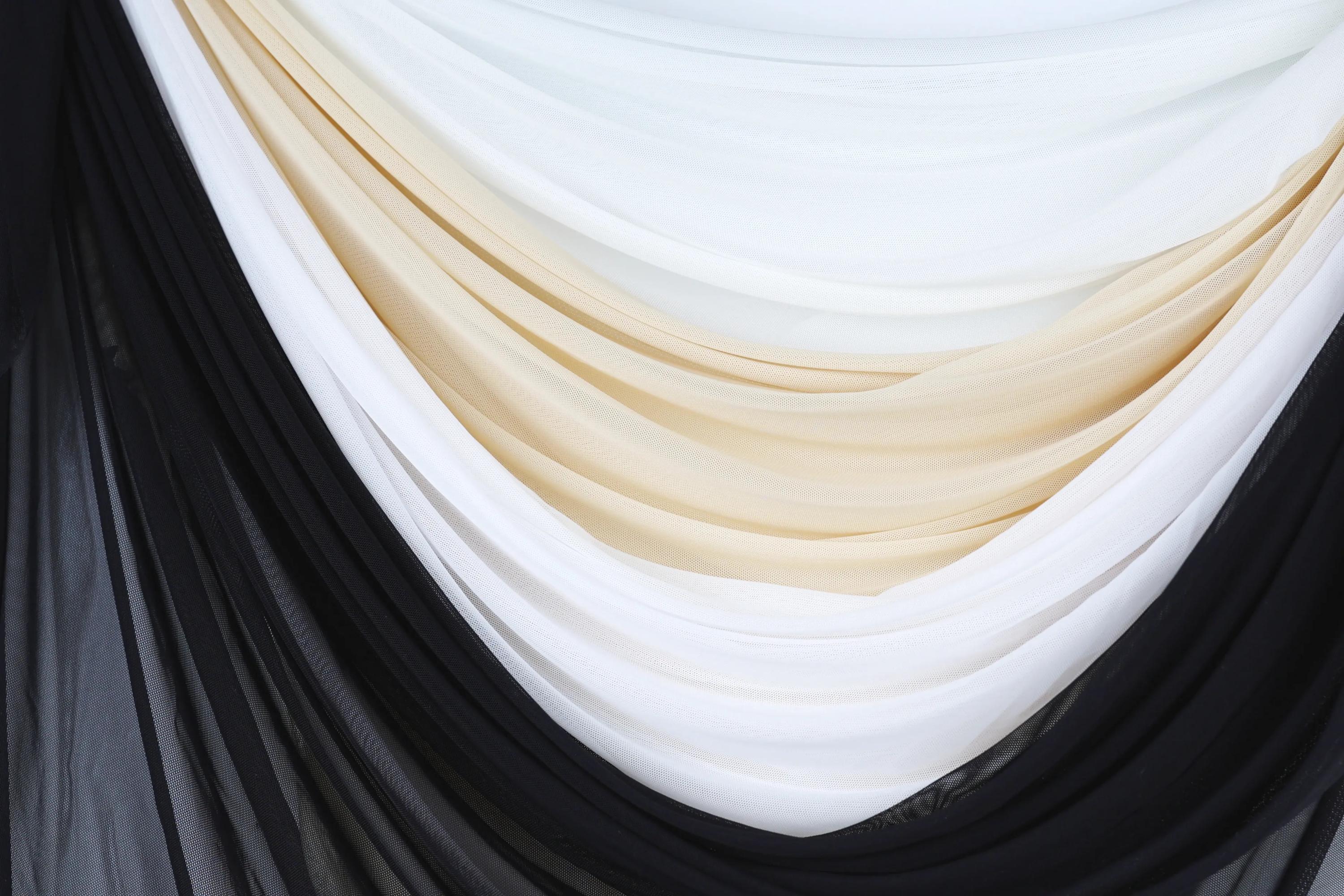a close-up view of a fabric with a layered design, consisting of black, white, and beige colors. The fabric appears to be draped or folded in a way that creates a visually appealing pattern.