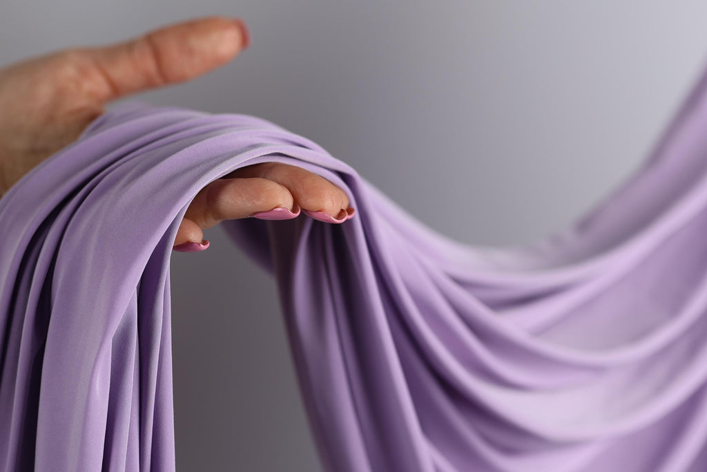 A hand with painted fingernails is holding a purple fabric, which appears to be a flowing garment or garment.