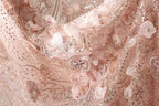 The image is a close-up of a delicate, intricately embroidered fabric with a floral pattern. The fabric appears to be made of a soft, light pink material and is adorned with numerous small, sparkling embellishments that add a touch of elegance and sophistication to the design.