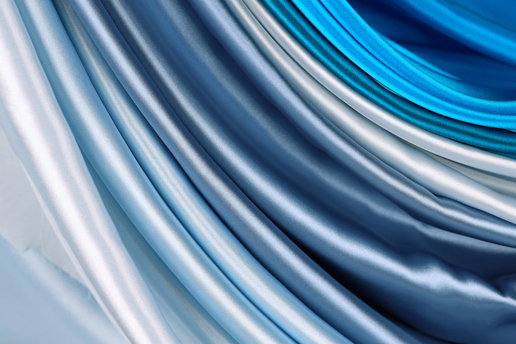 a close-up view of a collection of blue and silver fabric swatches, showcasing the smooth and shiny texture of the materials.