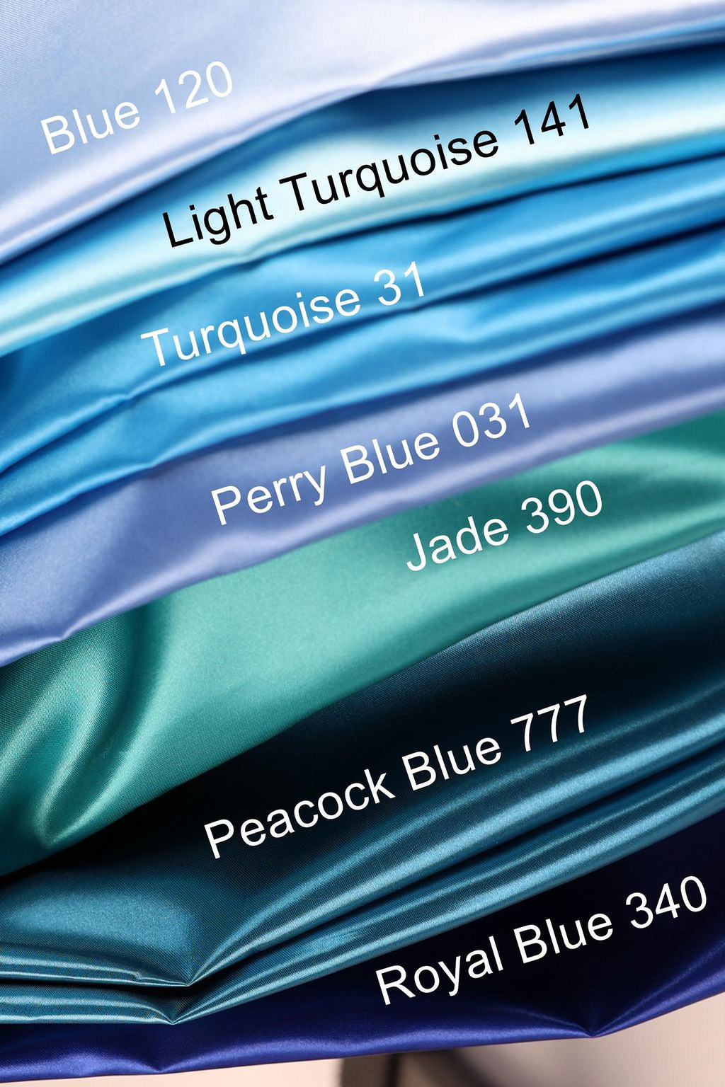 A close-up view of a stack of various colored silks, including turquoise, light turquoise, jade, royal blue, and peacock blue.