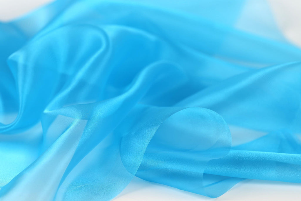 The image is a close-up of a blue fabric, possibly silk or chiffon, with a soft, flowing texture.