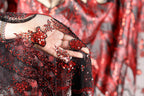 A close-up view of a hand holding a piece of red and black sequined fabric, with the fabric's intricate patterns and designs visible.