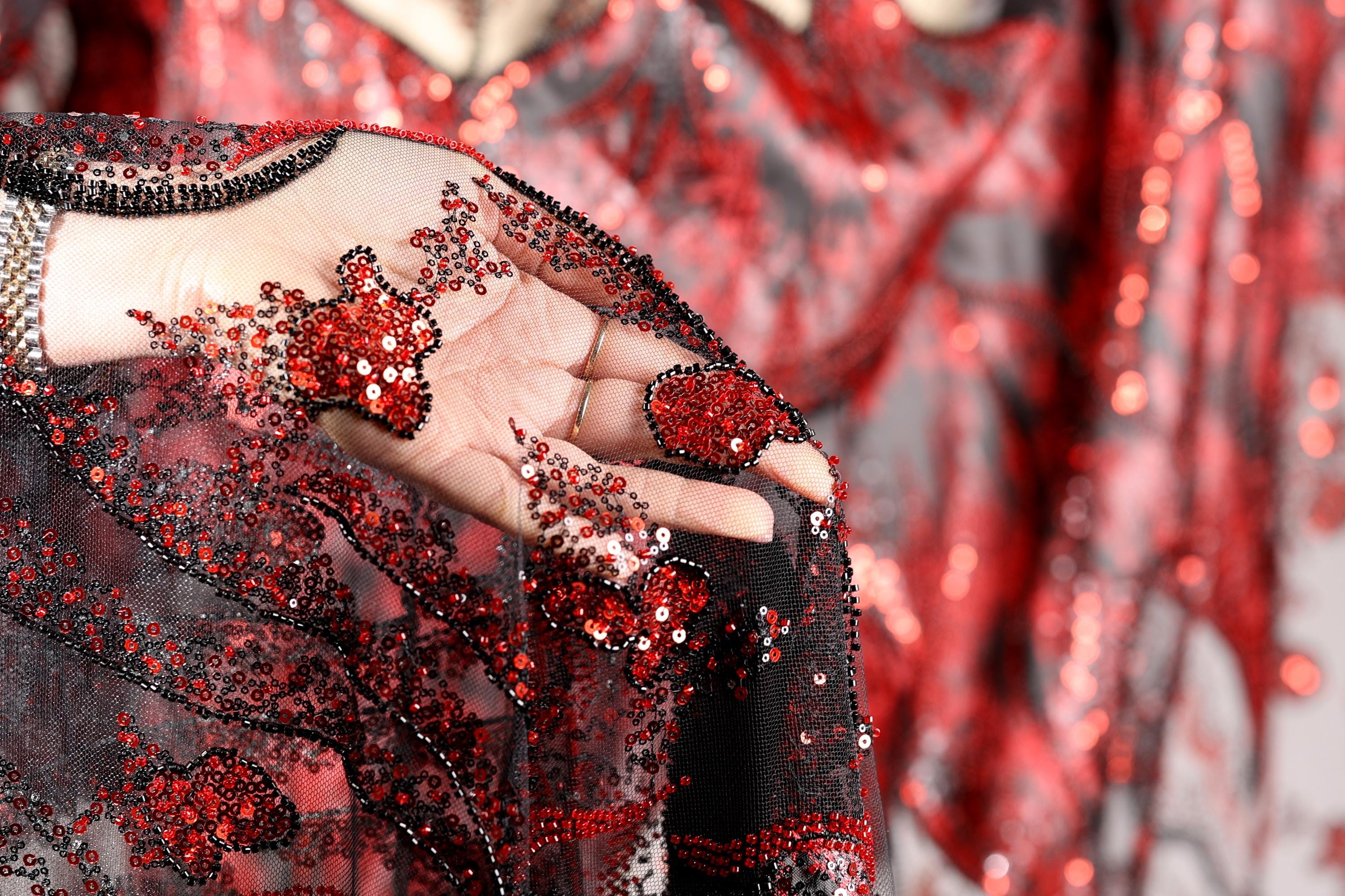 A close-up view of a hand holding a piece of red and black sequined fabric, with the fabric's intricate patterns and designs visible.
