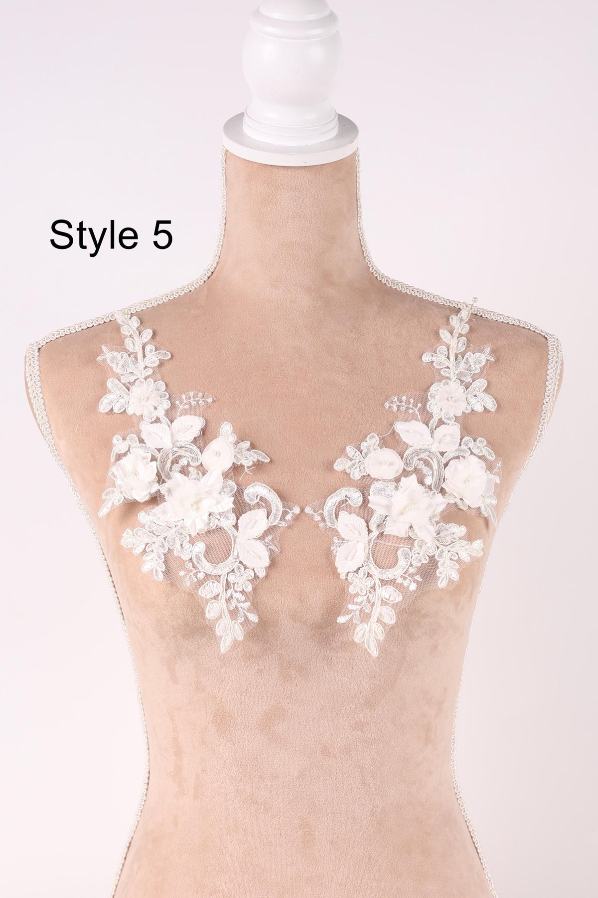 A mannequin wearing a white lace bodice with floral appliques on the shoulders.