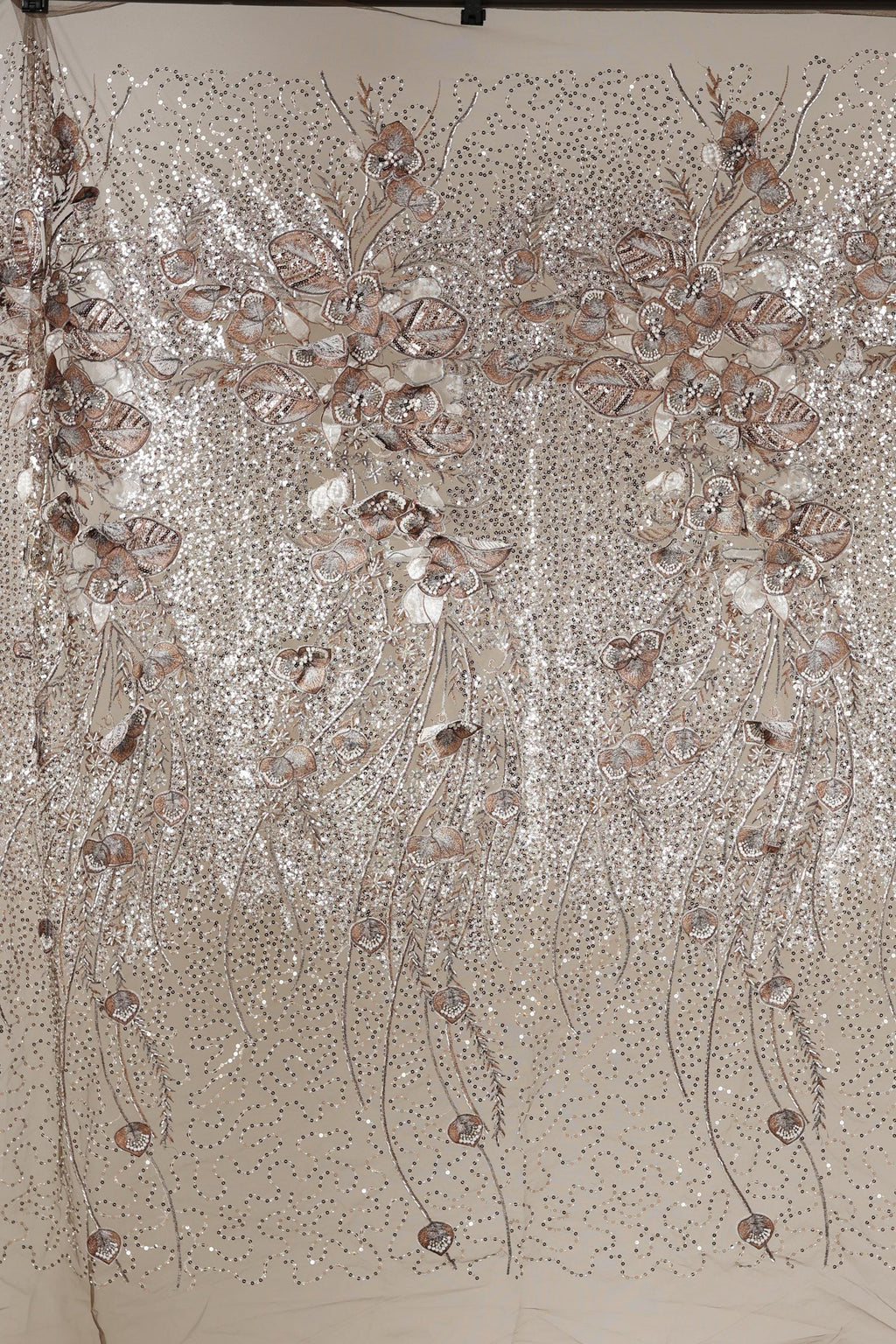 a close-up view of a fabric with a floral pattern, including various shades of pink and white flowers and leaves. The fabric appears to be made of a shiny, sequined material, giving it a sparkling and elegant appearance.