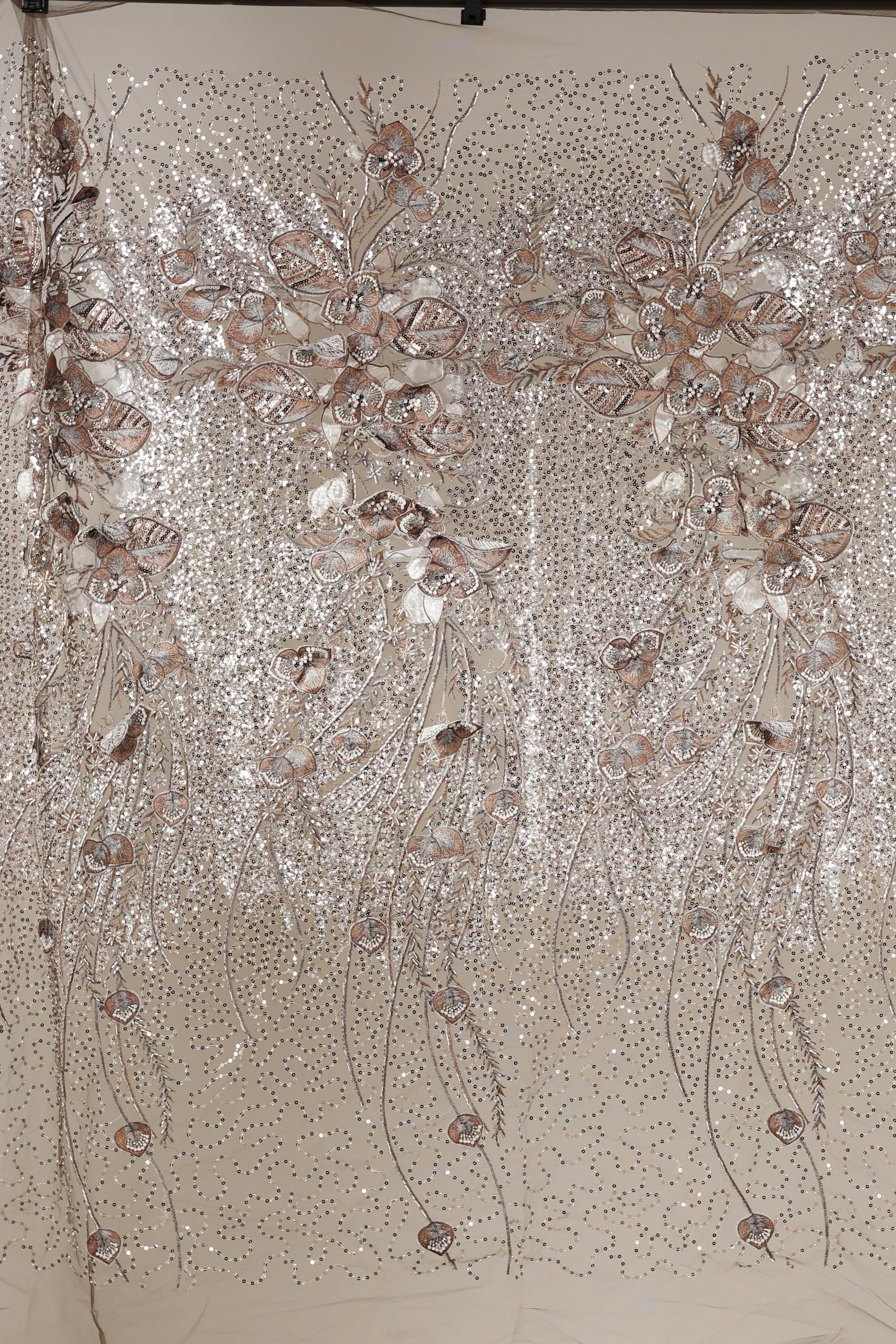 a close-up view of a fabric with a floral pattern, including various shades of pink and white flowers and leaves. The fabric appears to be made of a shiny, sequined material, giving it a sparkling and elegant appearance.