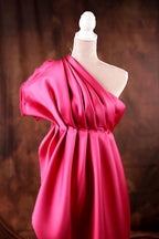 A pink one-shoulder dress displayed on a mannequin against a brown background.