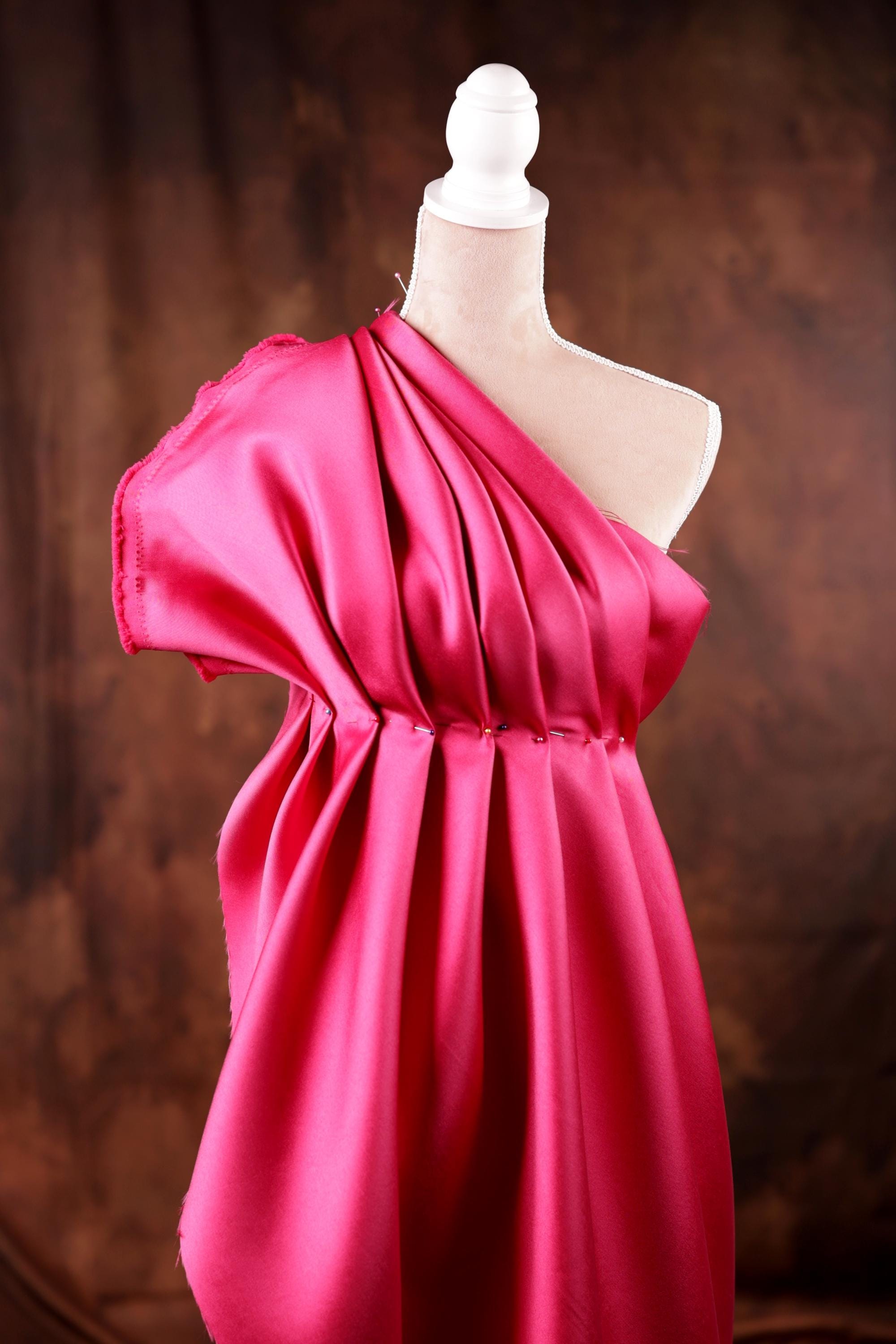 A pink one-shoulder dress displayed on a mannequin against a brown background.