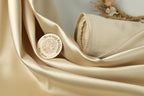 a close-up of a piece of gold-colored fabric with a circular logo or emblem on it, placed on a surface with a floral arrangement in the background.