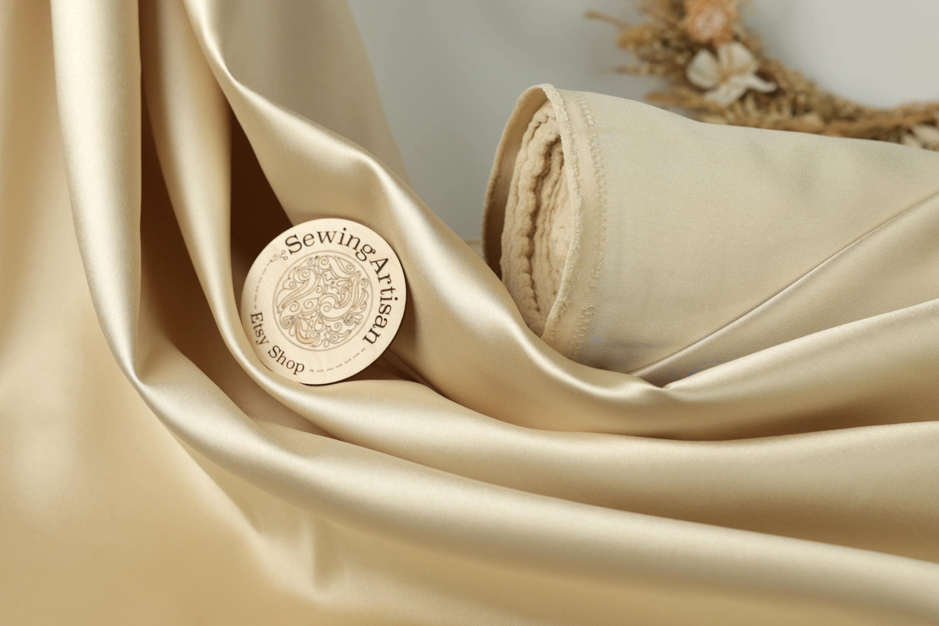 a close-up of a piece of gold-colored fabric with a circular logo or emblem on it, placed on a surface with a floral arrangement in the background.