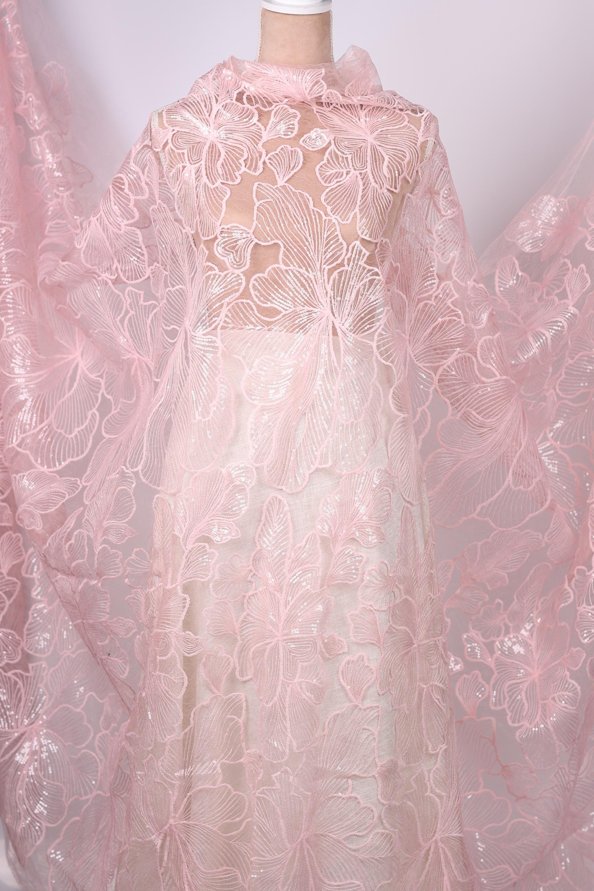 a close-up view of a delicate, pink lace fabric with intricate floral patterns. The fabric appears to be a sheer, sheer lace material, which is often used for creating dresses or other delicate garments. The image does not contain any text or other discernible objects, and the focus is solely on the lace fabric.