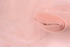 A close-up view of a soft, light pink fabric, possibly tulle, with a delicate, flowing texture.
