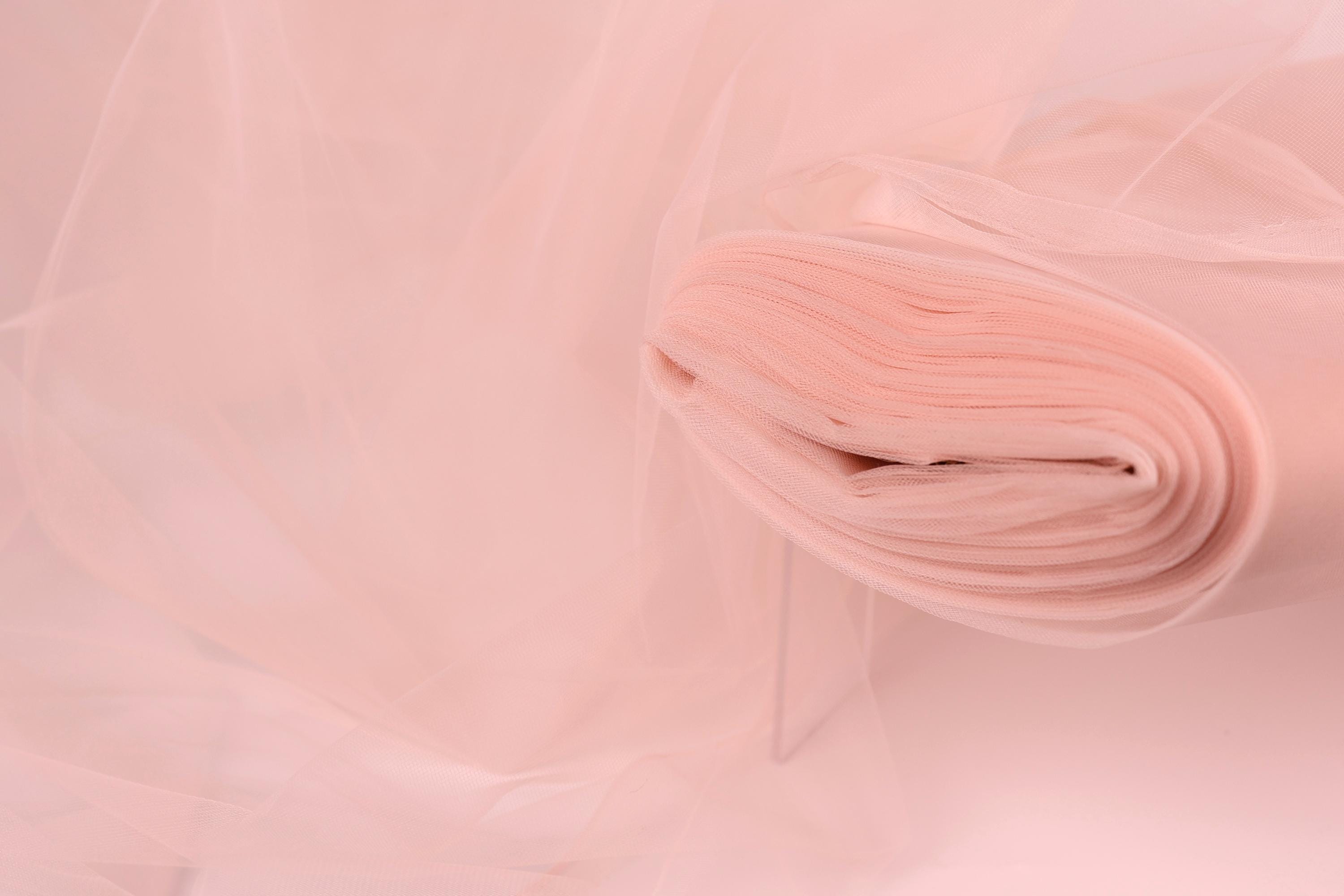 A close-up view of a soft, light pink fabric, possibly tulle, with a delicate, flowing texture.