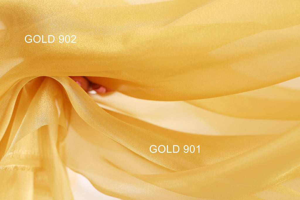 a close-up view of a flowing, golden fabric, possibly silk or chiffon, with the text "GOLD 902" and "GOLD 901" visible, indicating the color of the fabric.
