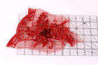 a close-up view of a red, intricately designed fabric with a floral pattern. The fabric appears to be a piece of lace or a similar type of textile, with a vibrant red color and a detailed, decorative design. The fabric is placed on a ruler, which is a common tool used in sewing and crafting to measure and cut fabric accurately.
