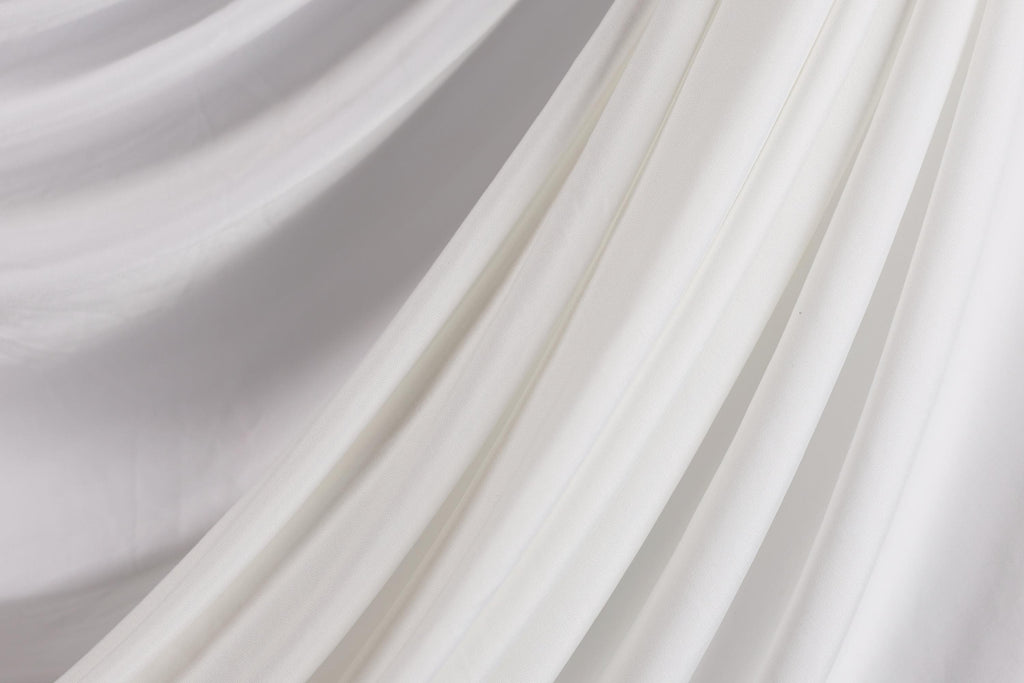 The image is a close-up of a white fabric, possibly a sheer or sheer-like material, with a soft, flowing texture.