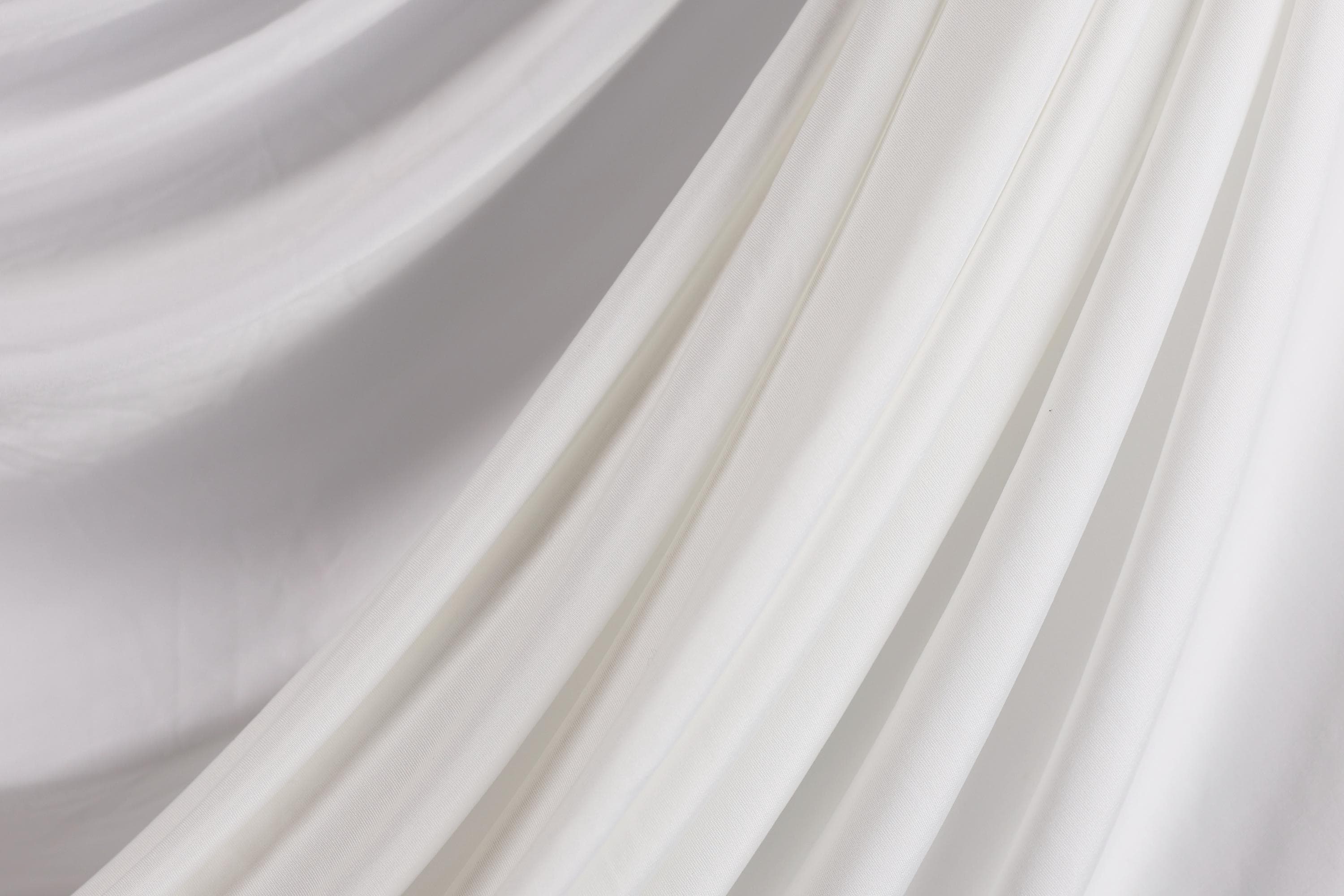 The image is a close-up of a white fabric, possibly a sheer or sheer-like material, with a soft, flowing texture.