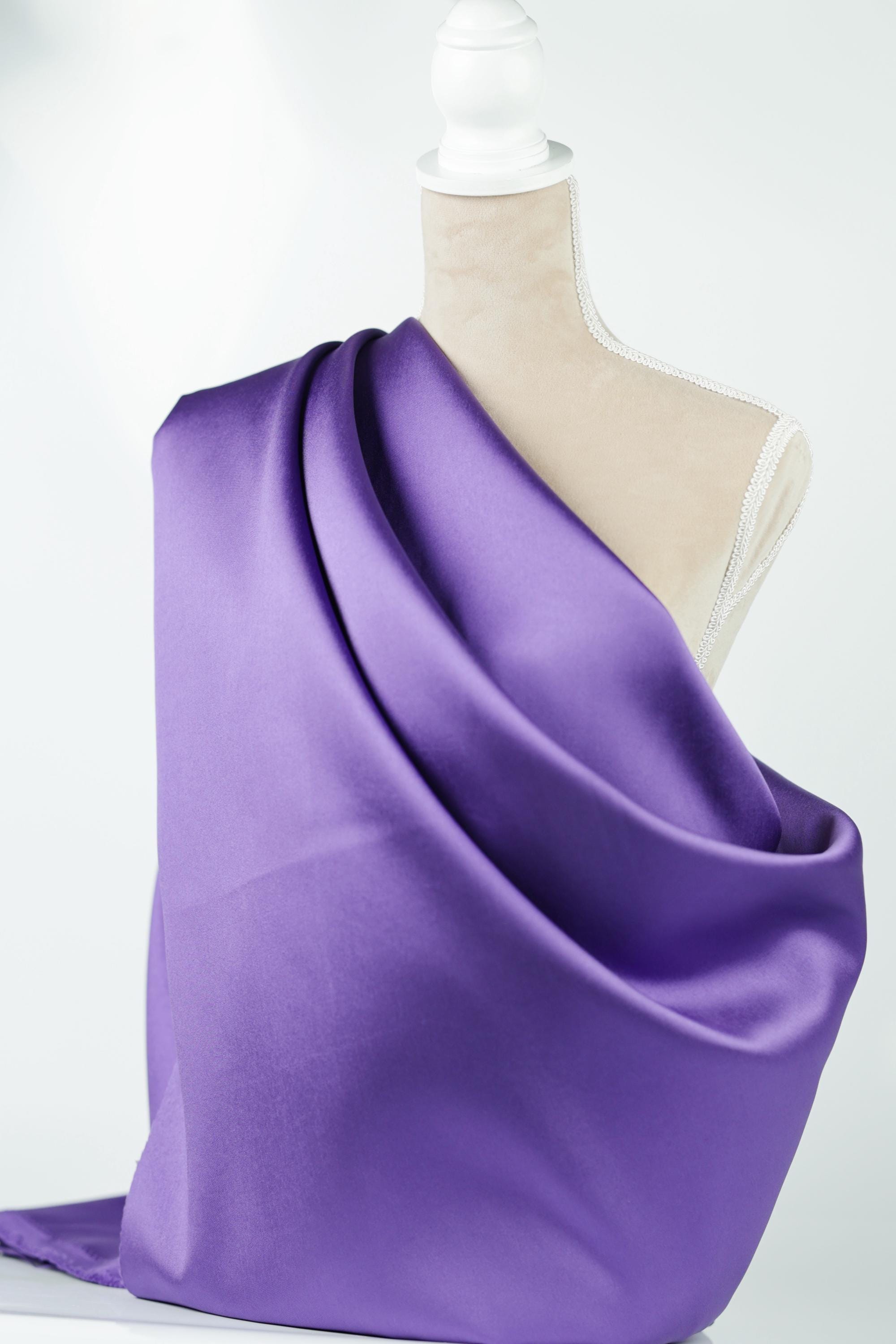 A mannequin is wearing a purple satin fabric draped over its body.