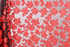 a close-up view of a fabric with a repeating pattern of red flowers on a white background. The flowers are arranged in a diagonal pattern, creating a visually striking contrast between the red and white colors. The fabric appears to be made of a sheer material, which adds a delicate and airy texture to the overall design.