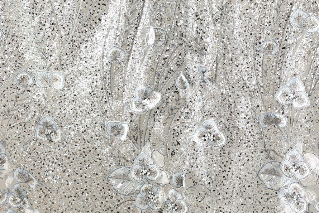 The image is a close-up of a fabric with a floral pattern, featuring small white flowers and leaves. The fabric appears to be made of a shiny, metallic material, giving it a sparkling and elegant appearance.