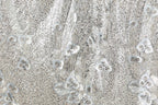 The image is a close-up of a fabric with a floral pattern, featuring small white flowers and leaves. The fabric appears to be made of a shiny, metallic material, giving it a sparkling and elegant appearance.