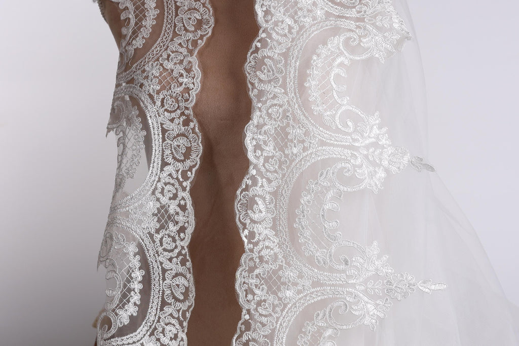 A close-up view of a delicate, white lace wedding veil with intricate floral patterns.