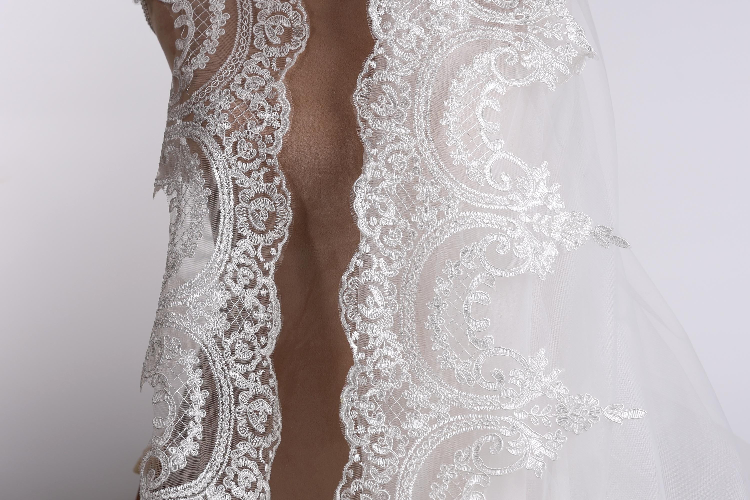 A close-up view of a delicate, white lace wedding veil with intricate floral patterns.