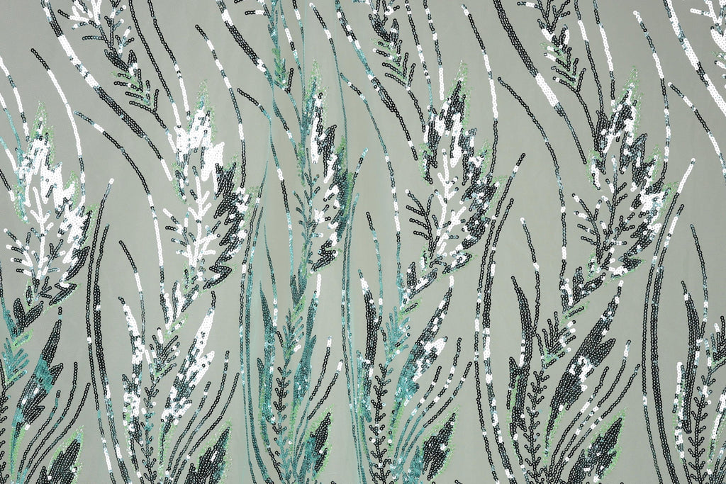 a close-up view of a fabric with a repeating pattern of green and white sequin designs resembling grass or plants. The pattern is intricate and detailed, with the sequins arranged in a way that creates a sense of movement and texture. The overall color scheme is predominantly green and white, with some black and gray accents. The image does not contain any text or other discernible objects, and the focus is solely on the detailed pattern of sequins.