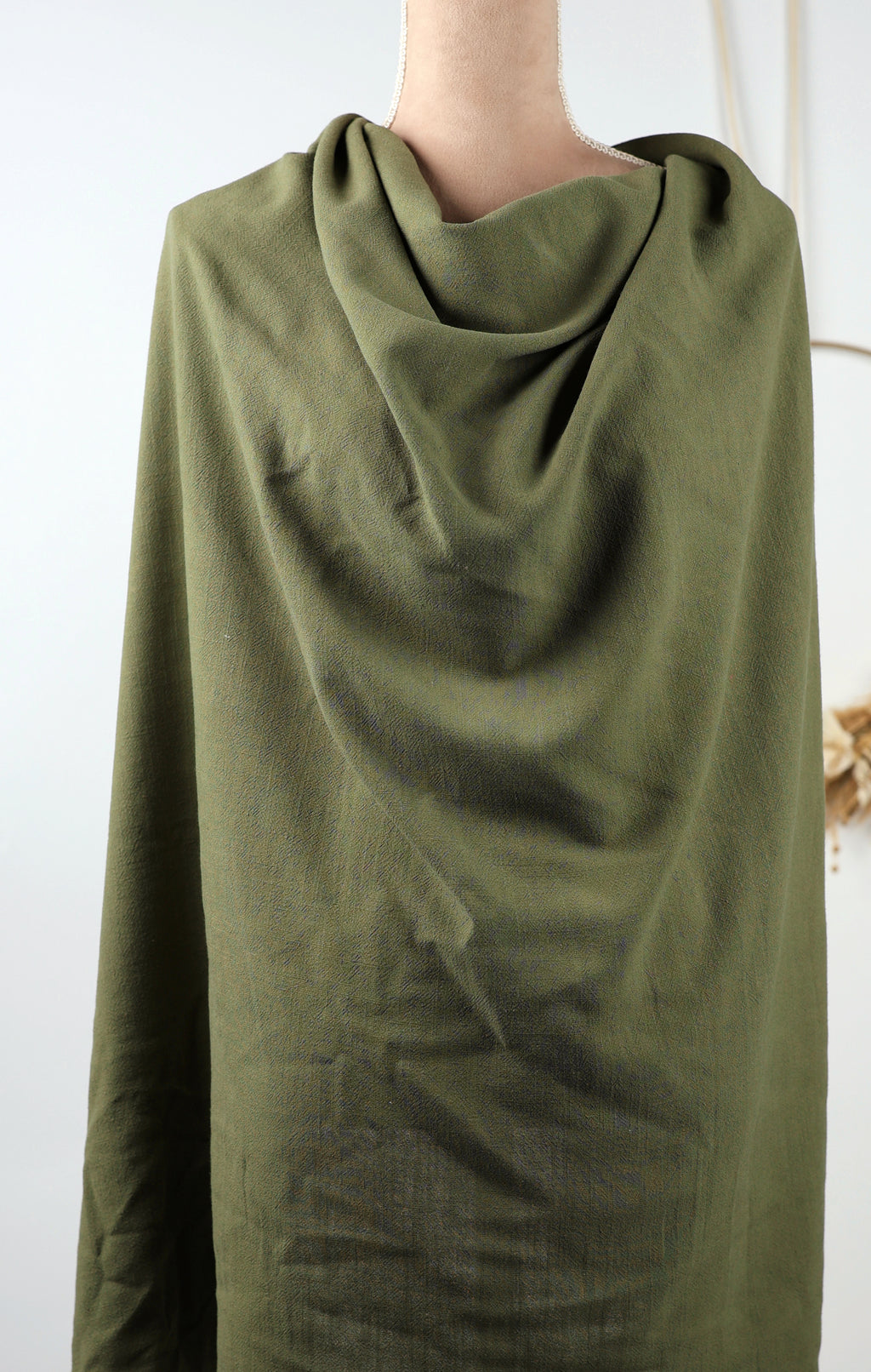 A mannequin wearing a green, loose-fitting garment with a draped, flowing appearance.