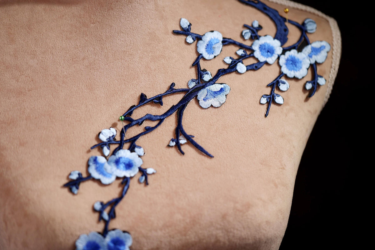 a close-up view of a delicate blue floral embroidery on a fabric, with the flowers and branches intricately detailed and sewn onto the fabric.