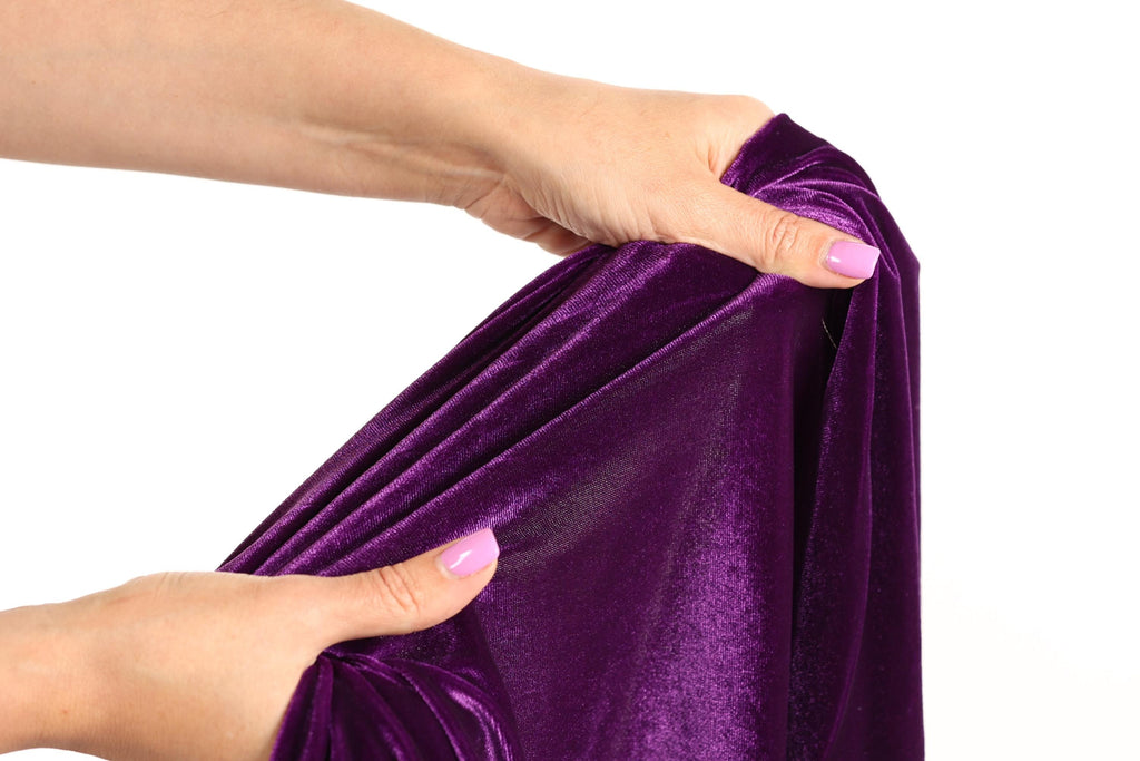 A hand is holding a purple velvet fabric, examining it closely.