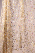 a delicate, floral-patterned fabric with a beige color. The fabric is adorned with numerous small, colorful flowers and leaves, creating a visually appealing and intricate design. The fabric appears to be a sheer or sheer-like material, which adds to its delicate and ethereal appearance.