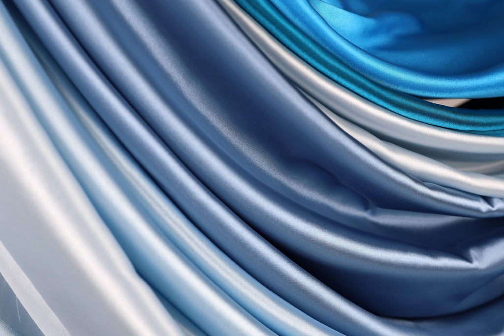 a close-up view of a collection of blue and silver satin fabric, with the fabric appearing to be folded or draped in a way that creates a sense of depth and texture.