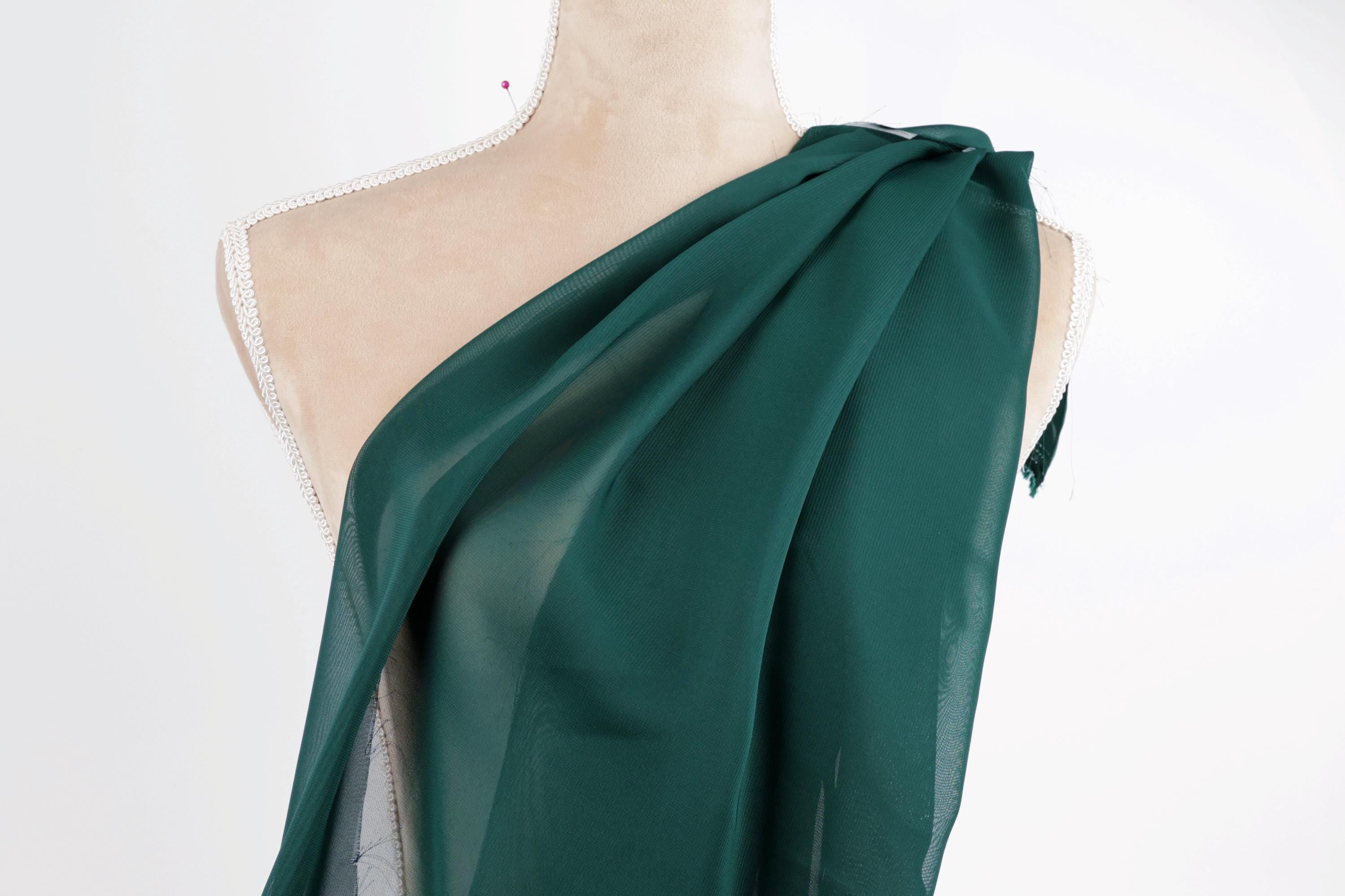 A mannequin wearing a green draped fabric draped over its shoulder.