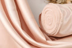 A close-up image of a soft, light pink satin fabric, possibly a satin curtain or fabric, with a rolled-up end visible.