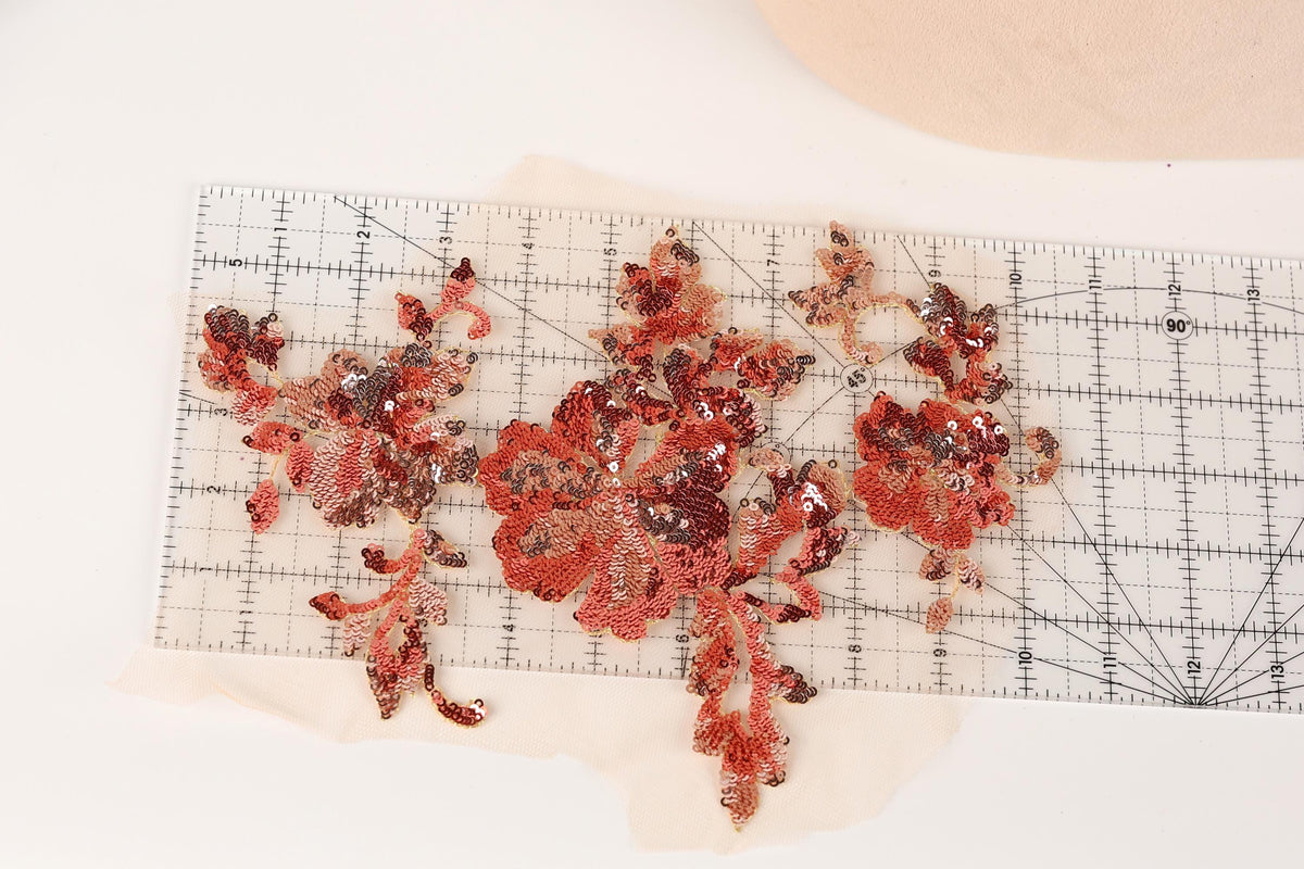 a clear ruler with red sequin flower-shaped pieces placed on it, indicating a sewing or crafting project.