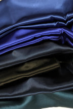 a close-up view of a stack of various colored satin fabrics, including shades of blue, black, and green.