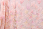 a close-up view of a fabric with a floral pattern in shades of pink and peach. The fabric appears to be made of sheer material, with a delicate and intricate design.