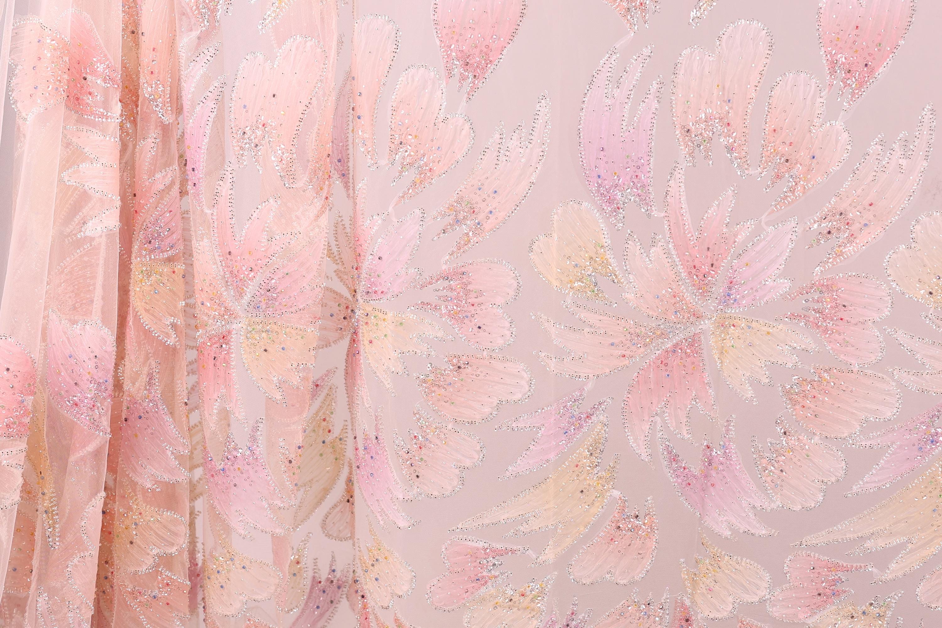 a close-up view of a fabric with a floral pattern in shades of pink and peach. The fabric appears to be made of sheer material, with a delicate and intricate design.