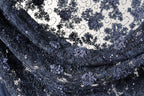 The image is a close-up view of a fabric with a floral pattern, featuring a mix of dark blue and black colors. The fabric appears to be made of lace or a similar material, with intricate details and embellishments.