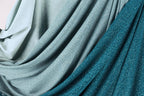 a close-up view of a fabric with a shimmering, sparkly texture in shades of blue and gray. The fabric appears to be made of a shiny, metallic material, giving it a unique and eye-catching appearance.