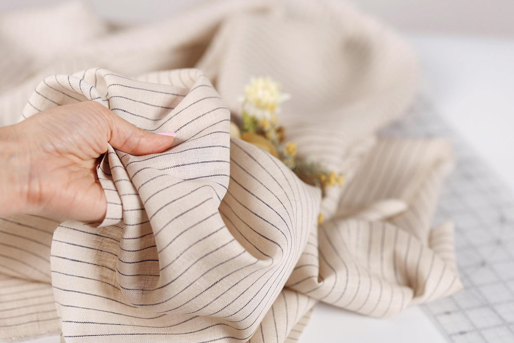 A hand is holding a piece of fabric with black and white striped patterns, with a small flower visible in the background.